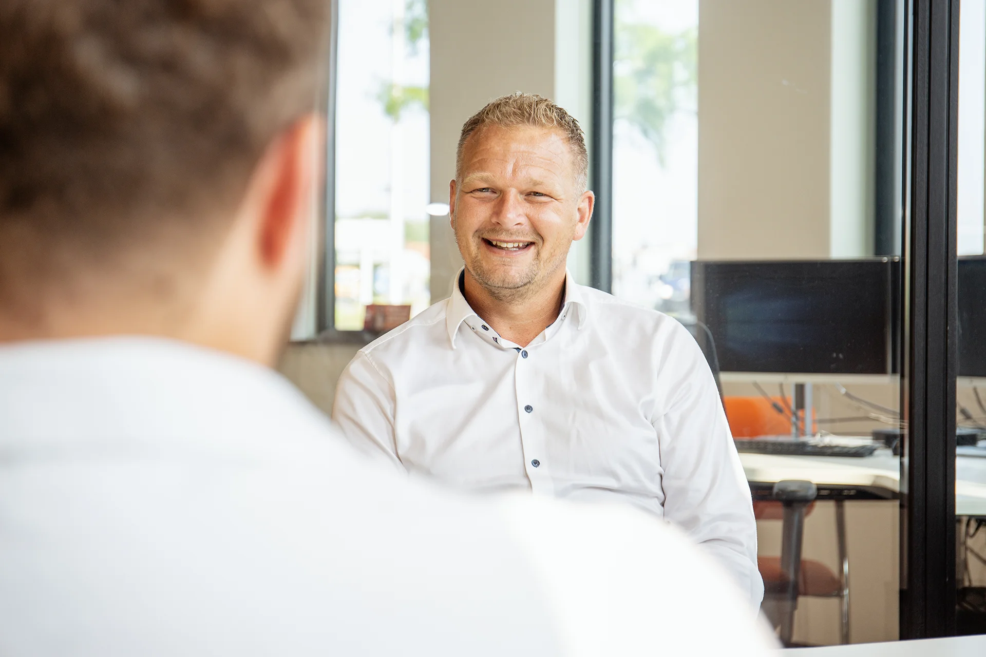 Lachende collega in gesprek met andere collega. De andere collega is vanaf de achterkant te zien