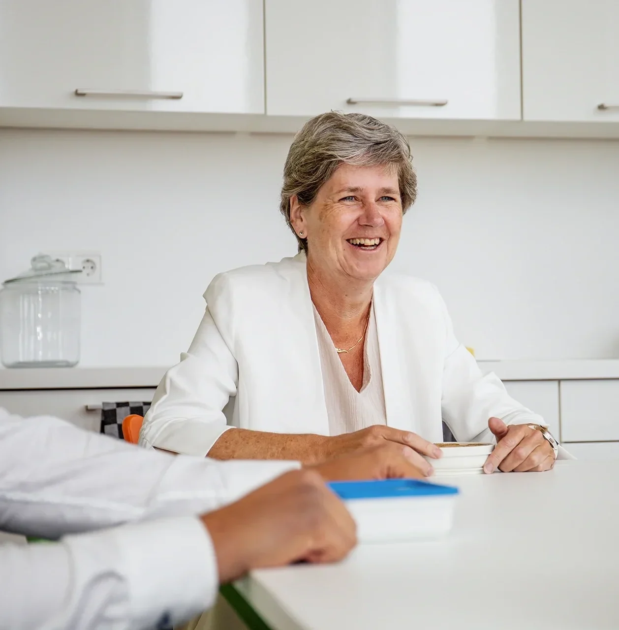 Mariet lacht in de keuken met collega's tijdens de pauze